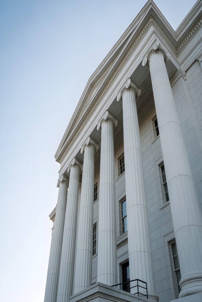 White neoclassical building façade with tall columns and decorative pediment against a blue sky.