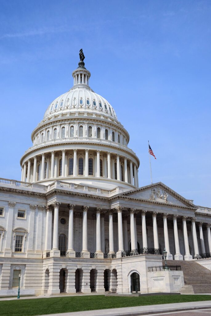 Front view of the U.S. Capitol with its white dome, statue atop, and rows of neoclassical columns against a blue sky.